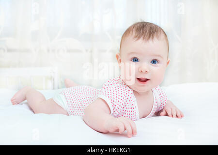 Cute baby smiling while lying on a white bed Stock Photo