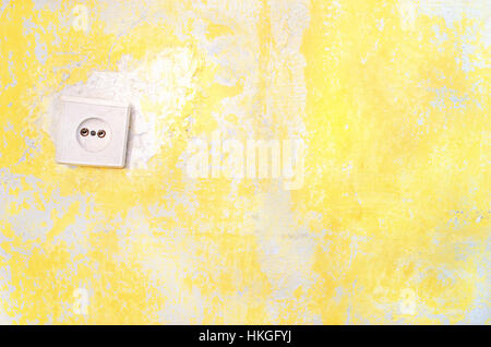 Wall socket on the yellow old plastered wall whith copyspace. Old electrical outlet on a decrepit wall. Fragment of a old wall with electrical socket Stock Photo