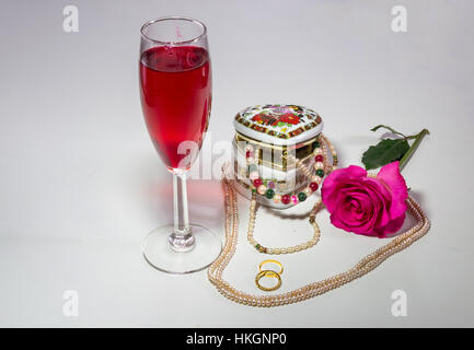 Romantic content with heart shaped artistic jewelry box with pearl necklaces red wine glass pink rose and engagement rings. Stock Photo