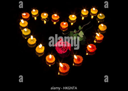 Romantic Valentines day setup with lighted candles in heart shape and a red rose isolated in black background - love relationship. Stock Photo