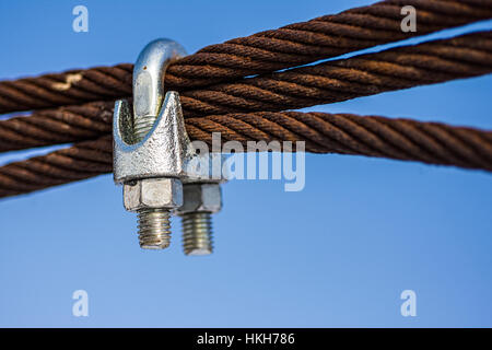 Rusty Steel Ropes with Shiny U-Bolt Clamp on Blue Sky Background. Business Teamwork Support Together Concept. Stock Photo