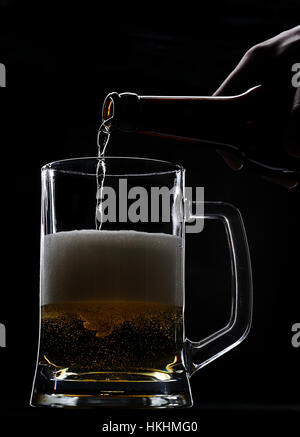 Pouring fresh beer from bottle on black Stock Photo