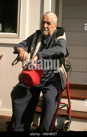 old man sitting on his walker to rest in the shade during a Summer ...