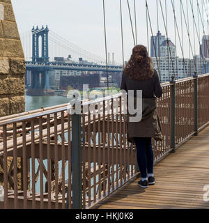 A young woman stands on the Brooklyn Bridge looking out over the East River to the Manhattan Bridge; New York City, New York, United States of America Stock Photo