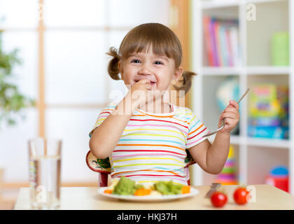 Funny little girl eating healthy food in kindergarten Stock Photo