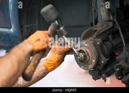 Close up view of incognito mechanic hands in dirty orange gloves trying to unscrew the nut with hammer of wheel mechanism Stock Photo