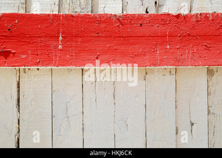 Horizontal red stripe of painted wooden board against white fence covered with cracked peeled old paint. Background concept with copy space Stock Photo