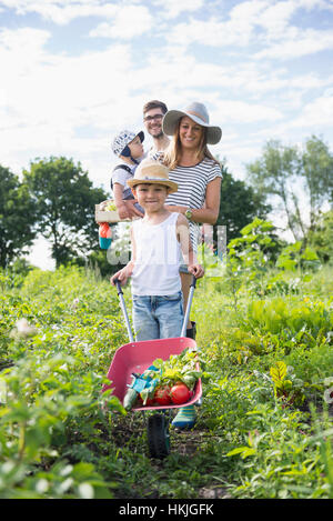 Family walking with wheelbarrow in community garden, Bavaria, Germany Stock Photo