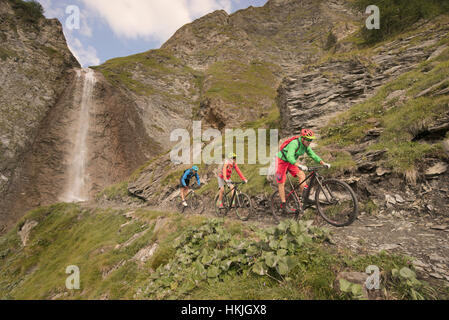 Three mountain bikers riding on hill at waterfall, Zillertal, Tyrol, Austria Stock Photo