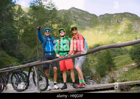 Three mountain biker friends standing on footbridge and showing something to his friends, Zillertal, Tyrol, Austria Stock Photo