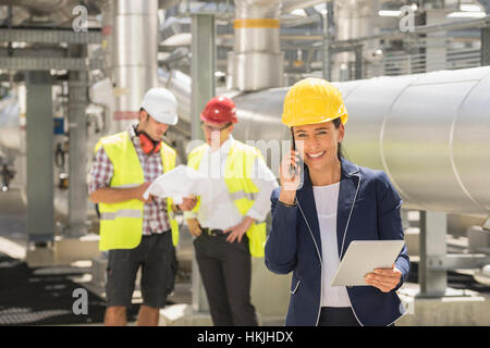 Female engineer talking on mobile phone with her colleague discussing in background, Bavaria, Germany Stock Photo