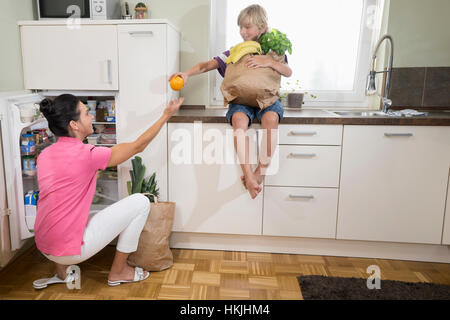 Boy giving an orange to his mother at refrigerator,Bavaria,Germany Stock Photo