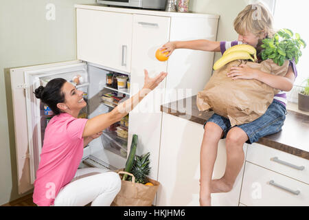 Boy giving an orange to his mother at refrigerator,Bavaria,Germany Stock Photo