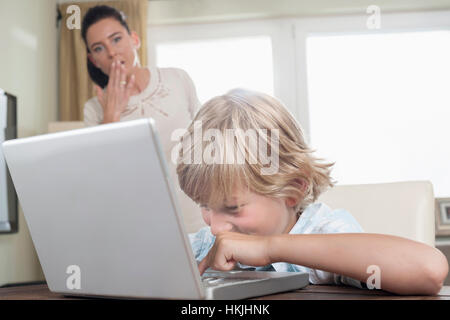 Shocked woman watching her son using laptop in living room,Bavaria,Germany Stock Photo