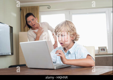 Shocked woman watching her son using laptop in living room,Bavaria,Germany Stock Photo