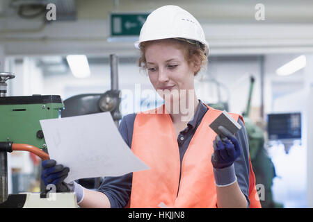 Young female engineer holding machine part with paper in an industrial plant, Freiburg im Breisgau, Baden-Württemberg, Germany Stock Photo