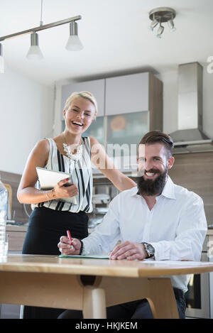 Portrait of a young couple with digital tablet in the kitchen and smiling, Bavaria, Germany Stock Photo