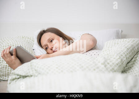 Pregnant woman lying in bed and using digital tablet, Munich, Bavaria, Germany Stock Photo