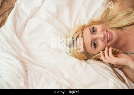 Portrait of a beautiful young woman talking on smart phone in the bedroom, Bavaria, Germany Stock Photo