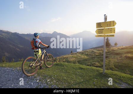Rear view of mountain biker standing in the alpine landscape and looking at view during sunset, Zillertal, Tyrol, Austria Stock Photo