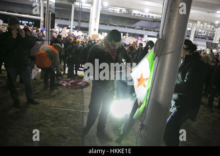 Chicago, USA. 28th Jan, 2017. Two men trying to attach a Free Syrian flag to a flag pole after the American flag was taken down by others. Protestors were gathering on front of Terminal Five at O'Hare International Airport, where some foreign refugees were being held, due to President Trump's immigration ban. Credit: Rick Majewski/ZUMA Wire/Alamy Live News Stock Photo