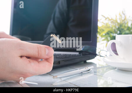 Man's hand is holding SD card against laptop Stock Photo