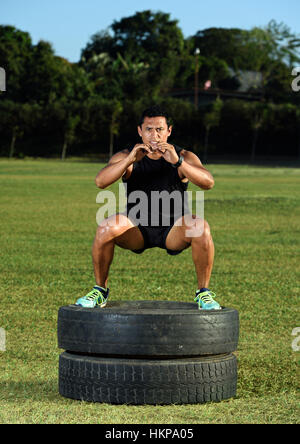 sporty guy working out on tire on green stadium grass Stock Photo
