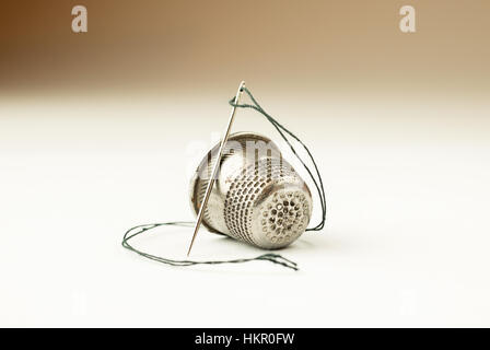 Metal thimble and needle with thread on over white Stock Photo