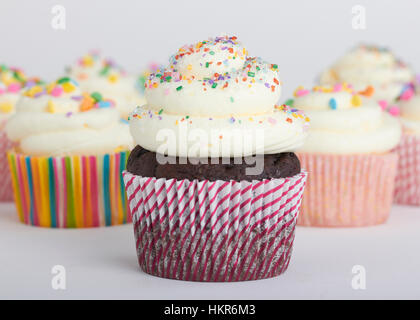 A dozen chocolate and white cupcakes with vanilla frosting and multi colored sprinkles. The cupcake wrappers have interesting and mixed prints/pattern Stock Photo