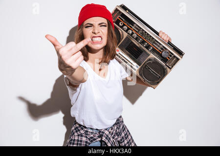 Image of young angry woman dressed in white t-shirt standing isolated over white background while holding tape recorder and showing middle finger to c Stock Photo