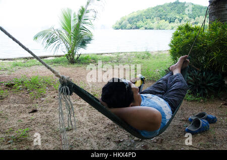 Asian thai man sleep and relaxing on furniture Hammock hanging between palm trees in garden of resort front of the beach and tropical sea water at Ko Stock Photo