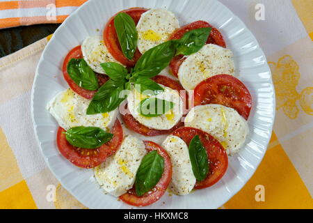 Tomato and buffalo mozzarella Caprese salad on colorful kitchen cloths - Prepared Italian recipe served in white dish - View from above - Summer salad Stock Photo