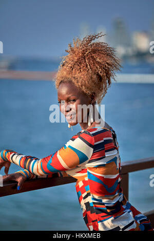 Portrait of a beautiful young African female with a tied up orange Afro Caribbean frizzy hairstyle and wearing a striking multi coloured dress. Stock Photo