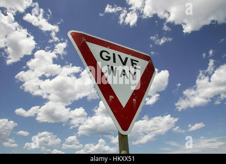 Give way traffic sign in front of blue sky with white clouds Stock Photo