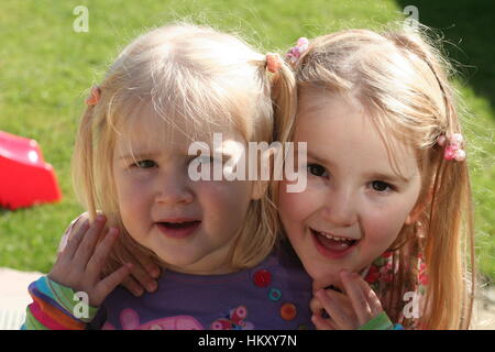 Little blonde girls, children kids wearing pigtails smiling hugging, sibling love, family love concept, connection, best friends concept, togetherness Stock Photo