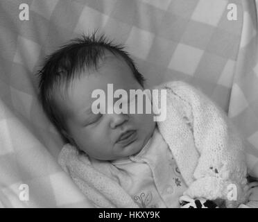 Newborn baby girl sleeping, content concept, new baby asleep, lots hair, sweet cute innocence, warm cosy cuddly, cardigan, precious delicate Stock Photo