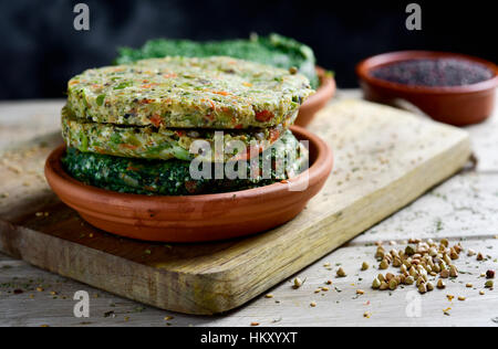 closeup of some different raw veggie burgers in an earthenware plate, on a rustic wooden table Stock Photo