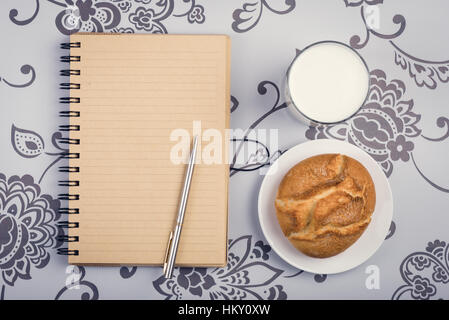 Roll, glass of milk or kefir and opened notepad with pen on the desktop Stock Photo