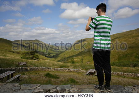 A young man in a green and white shirt takes a photograph of a valley in the West of Ireland Stock Photo
