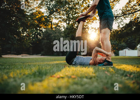 Side view of physical trainer helping woman do stretching workout. Personal trainer assisting woman in leg stretching workout. Stock Photo