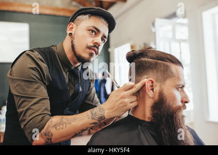 Barber checking symmetry of haircut of his client. Bearded man getting trendy haircut by hairstylist at barbershop Stock Photo