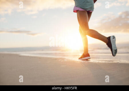 Feet of young woman jogging on the beach. Fitness female on morning run at sea shore. Stock Photo