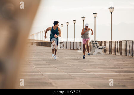 Two runner sprinting on road by the sea. Fitness couple running on the sea side promenade. Stock Photo