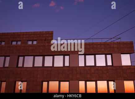 Building at dusk with colorful reflections in the windows against dark violet sky and pink clouds Stock Photo