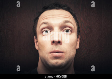 Young surprised Caucasian man. Close-up studio face portrait over dark wooden wall background, selective focus