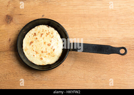 A freshly cooked pancake in a cast iron frying pan on a wooden board Stock Photo