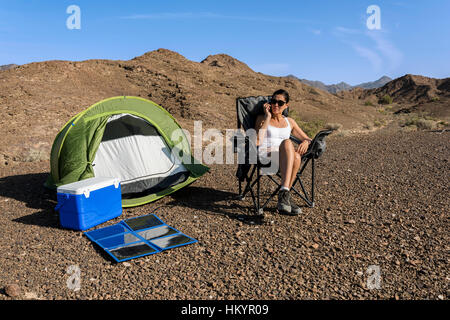 Woman in the desert calling while her smartphone is charging with a foldable solar panel. Stock Photo