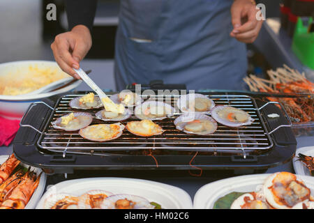 Man cooking the scallops and other seafood on grill barbecue, asia street food cuisine Stock Photo