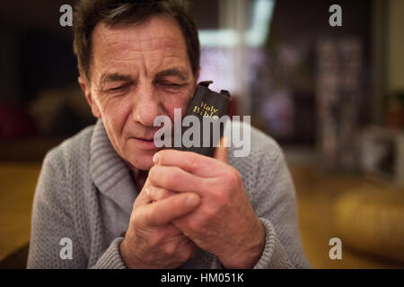Senior man praying, holding Bible in his hands, eyes closed. Stock Photo