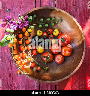 Variety of heirloom tomatoes in a rustic bowl and on a light wood surface Stock Photo